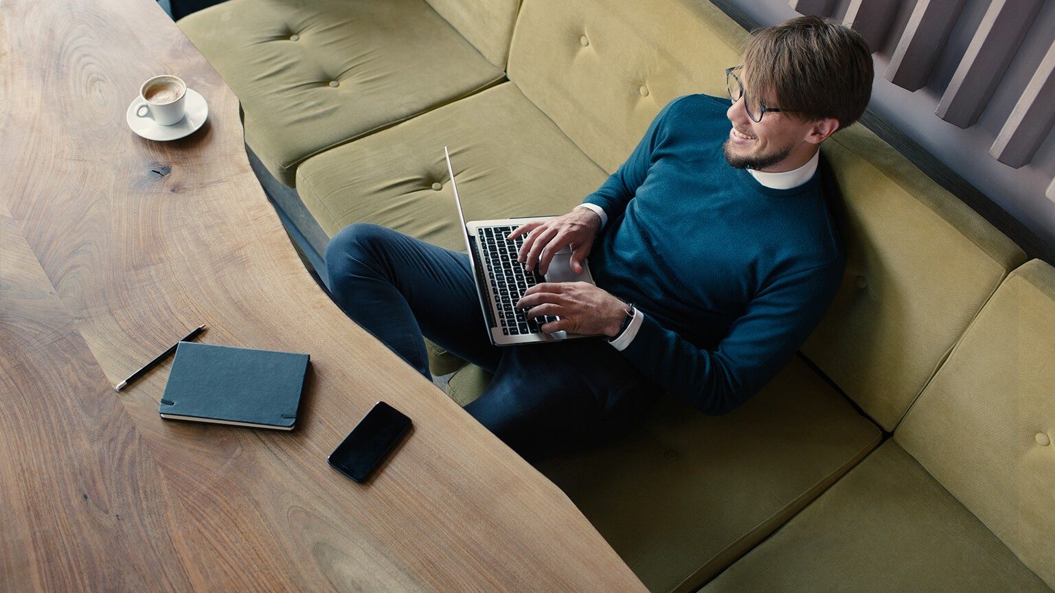 Junger Mann sitzt auf seinem Sofa mit Brille und tippt in den Laptop